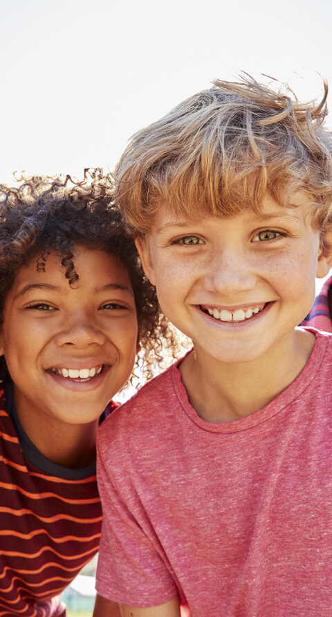 Two smiling children outdoors against white background, wearing casual colorful clothing.