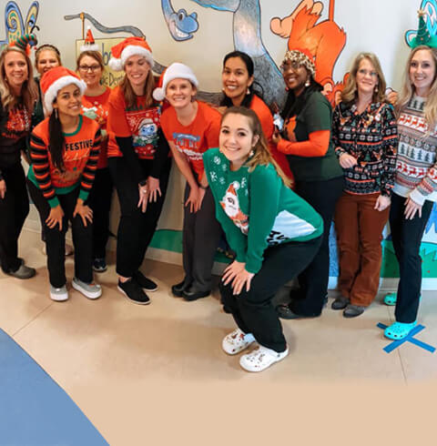 Group of children and staff in holiday attire at pediatric dental office celebration.