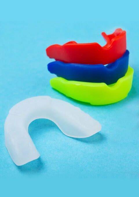 Colorful orthodontic retainers stacked on blue background, dental care equipment.